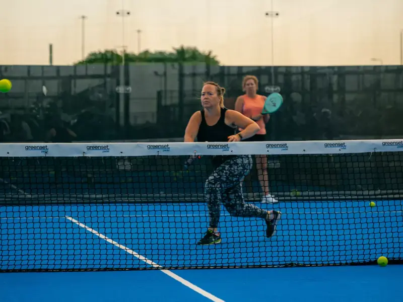 Woman running after a ball with her racket raised during a Padel game.